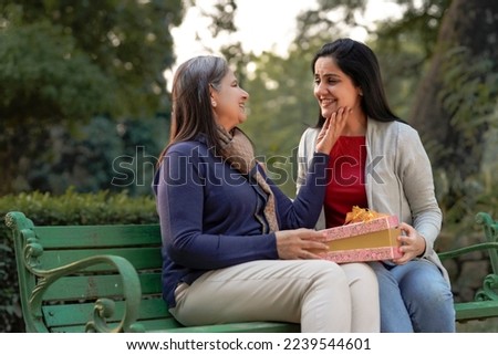 Young woman giving surprise gift to senior or old woman at park Royalty-Free Stock Photo #2239544601
