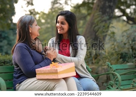 Young woman giving surprise gift to senior or old woman at park Royalty-Free Stock Photo #2239544609