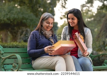 Young woman giving surprise gift to senior or old woman at park