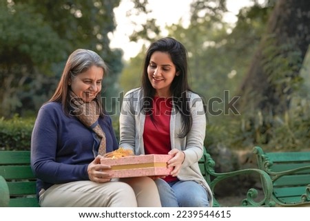 Young woman giving surprise gift to senior or old woman at park