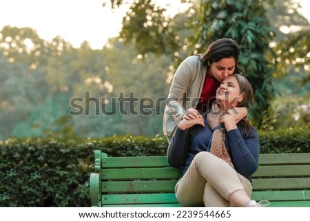 Two indian woman sitting at park in winter wear Royalty-Free Stock Photo #2239544665