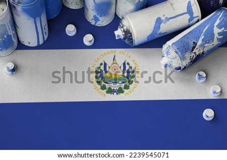 El Salvador flag and few used aerosol spray cans for graffiti painting. Street art culture concept, vandalism problems