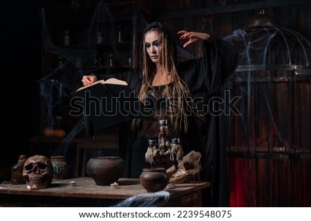 Witch dressed dark dungeon room use magic book for conjuring magic spell. Female necromancer wizard gothic interior with skull, cage, spider web