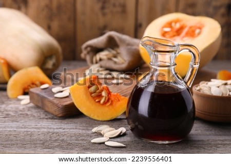 Fresh pumpkin seed oil in glass jug on wooden table. Space for text