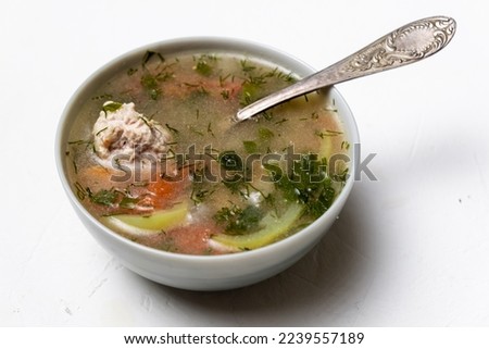 Vegetable soup with meatballs in a plate on a white background.