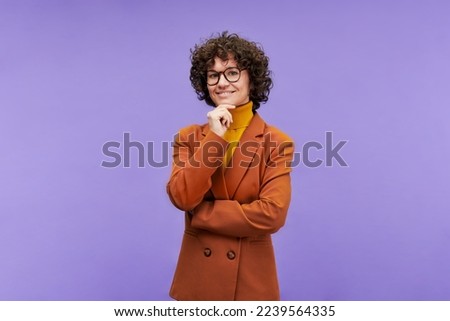 Happy young elegant teacher in stylish formalwear and eyeglasses standing in front of camera in isolation against violet background