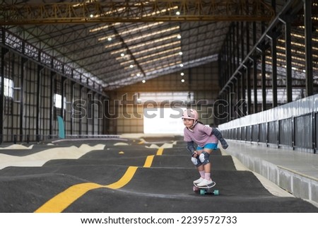 asian child skater or kid girl fun playing skateboard or ride surf skate in indoor pump track in skate park by extreme sports surfing to wearing helmet elbow pads wrist knee support for body safety Royalty-Free Stock Photo #2239572733
