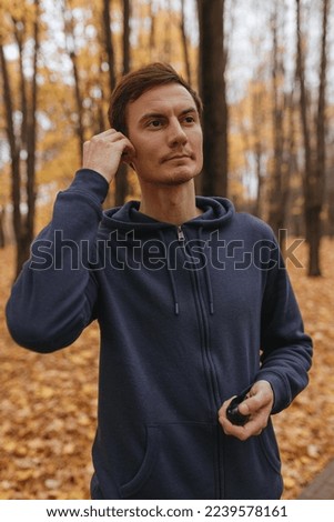Sportsman listening to music in wireless earphones during running training in autumn park 