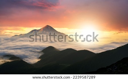Sunset landscape with high peaks and foggy valley with thick white clouds under vibrant colorful evening sky in rocky mountains. Royalty-Free Stock Photo #2239587289