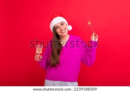 Christmas holidays. A beautiful brunette in a Santa Claus hat drinks champagne and holds a sparkler