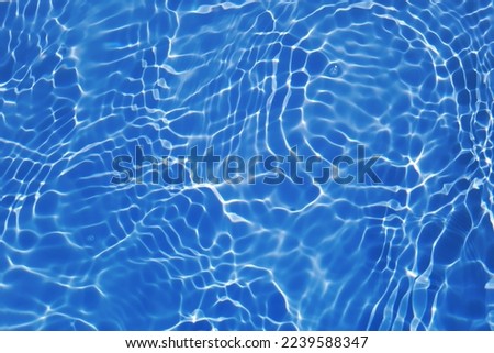 Defocus blurred transparent blue colored clear calm water surface texture with splashes and bubbles. Trendy abstract nature background. Water waves in sunlight with caustics. Blue water shinning  Royalty-Free Stock Photo #2239588347