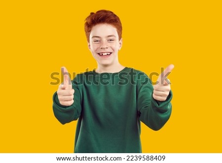 Portrait of happy, toothless, red-haired confident teenager in casual, warm, green sweater, looking and pointing fingers directly at you in the camera on an isolated yellow background.