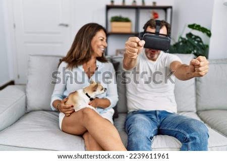 Middle age man and woman couple using vr goggles sitting on sofa with dog at home