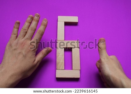 number six written with wood blocks on purple background and number 6 indicated by finger. number representation in sign language