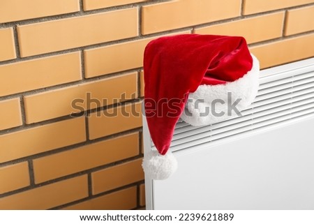 Santa hat on electric radiator near brick wall, closeup