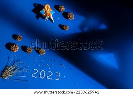 Happy new year 2023 on blue background, holidays card with lights, gifts and pine cone