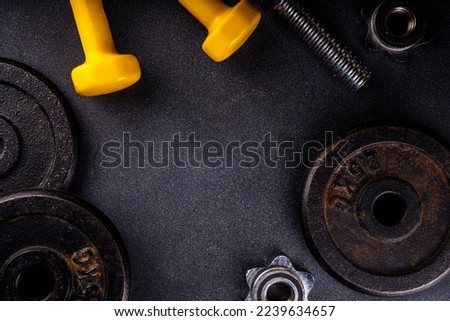 Fitness or bodybuilding background. Old hard iron dumbbells, small colorful dumbbells,  notepad with workout plan list. Back to gym concept, weight lifting sport flat lay top view copy space  