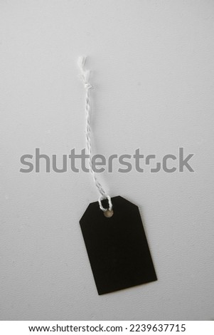 one blank hanging tags: empty eco friendly black made from recycled kraft paper at white table background. Recycle concept. Mock up. Blank black paper label. Photo with copy blank space. mockup.