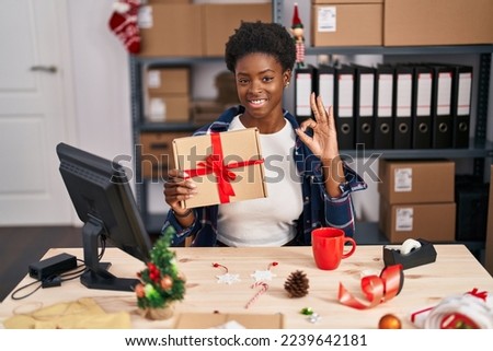 African american woman standing by manikin at small business on christmas doing ok sign with fingers, smiling friendly gesturing excellent symbol 