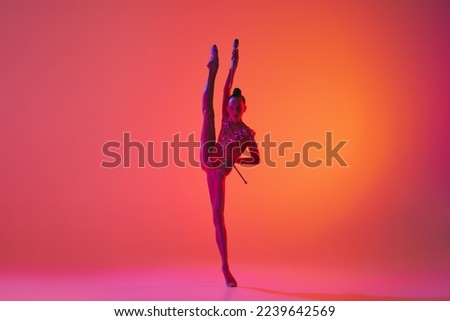 Beautiful and flexible graceful athlete rhythmic gymnastic artist dancing, doing stretch exercises isolated on colorful background in neon. Beauty, art, sport, competition, ad and hobbies concept