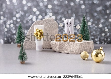 cartoon model of a tooth, the numbers 2023 on a podium made of stone, toothpaste and Christmas trees on a background of silver bokeh