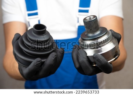 Car mechanic in blue jumpsuit holds in his hands hinge of equal angular velocities of car and puts another on it. Spare parts protection concept against dust and dirt. auto parts. Royalty-Free Stock Photo #2239653733