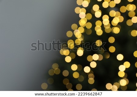 Blurred view of beautiful fir tree with Christmas lights on grey background, closeup. Space for text