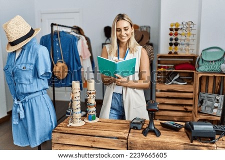 Young blonde woman smiling confident writing on notebook at clothing store