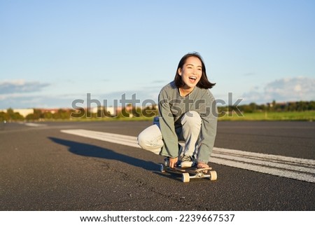 Freedom and happiness. Happy asian girl riding her longboard on an empty sunny road, laughing and smiling, skateboarding. Royalty-Free Stock Photo #2239667537