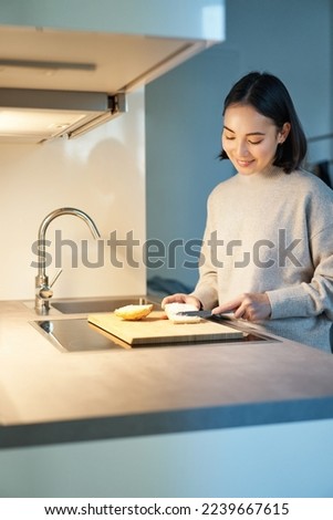 Vertical shot of young asian woman cooking dinner, making herself sandwitch, smiling while standing on the kitchen.