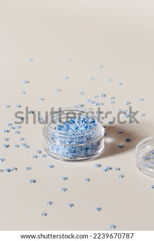 Elements for nails decor, small blue stars in glass box, stars for nail art in jar on beige background for promotion content. Minimal style aesthetic image, creative beauty concept, palm leaf shadow