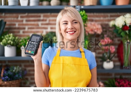 Young caucasian woman working at florist shop holding dataphone looking positive and happy standing and smiling with a confident smile showing teeth 