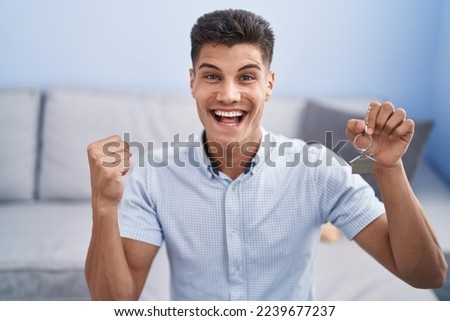 Young hispanic man holding keys of new home screaming proud, celebrating victory and success very excited with raised arm  Royalty-Free Stock Photo #2239677237