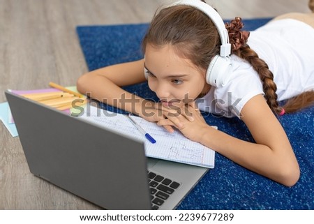 Close-up photo of a teenage girl lying on the floor listening to the school program at home online in front of a laptop monitor. Online education concept.