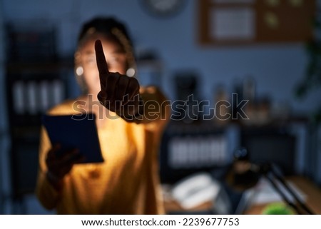 African american woman with braids working at the office at night with tablet pointing with finger up and angry expression, showing no gesture 