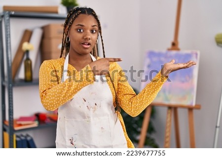 African american woman with braids at art studio amazed and smiling to the camera while presenting with hand and pointing with finger. 