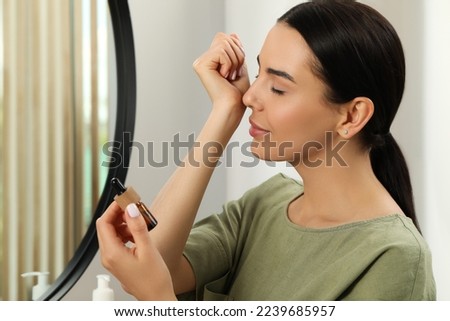 Young woman smelling essential oil on wrist indoors Royalty-Free Stock Photo #2239685957