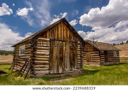 Some old log cabins standing beneath a beautiful summer sky in the Colorado high country. Royalty-Free Stock Photo #2239688319