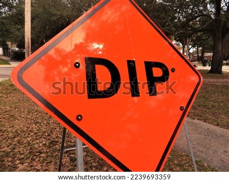 Orange traffic sign warning of dip in the road.