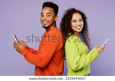 Young fun couple two friends family man woman of African American ethnicity wear casual clothes together hold in hand use mobile cell phone stand back to back isolated on plain light purple background