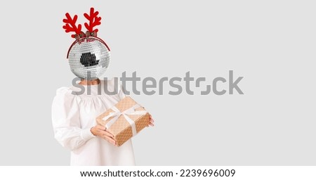 Woman with Christmas gift and disco ball instead of her head on light background with space for text