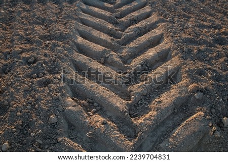 Close up and background of bare earth over which a tractor has driven. You can clearly see the tractor track on the right edge of the picture