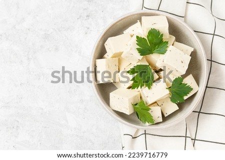Tofu soy cheese or paneer or feta cheese cubes adding fresh parsley and celery in a ceramic bowl on a checkered napkin isolated top view Royalty-Free Stock Photo #2239716779