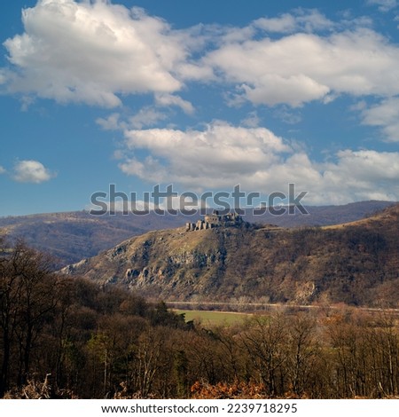 Medieval fortress on the hill of the mountain. Ruins of an old castle against a blue sky with clouds. Scenic view of the fortress mountain landscape in late autumn.
