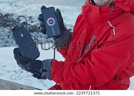 Charging a smartphone from a power bank against the backdrop of the sea and snow in winter