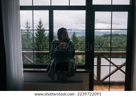Woman holding mug, sitting on windowsill and looking at mountains