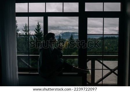 Silhouette of a woman sitting on the windowsill with a mug