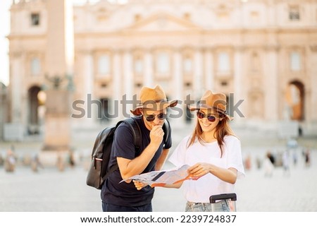Happy tourists looking at a map. Couple of tourists on vacation in Rome, Italy. A young couple of tourists choose a hotel. Honeymoon. Satisfied tourists looking for a direction on a map.  Royalty-Free Stock Photo #2239724837