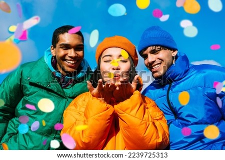 Multiracial group of young happy friends meeting outdoors in winter and celebrating party with confetti, wearing winter jackets and having fun - Multiethnic millennials bonding in a urban area Royalty-Free Stock Photo #2239725313