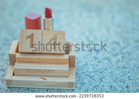 Stone background with the wooden calendar with the date of Valentine's Day put on it and with a red lipstick on the back.
